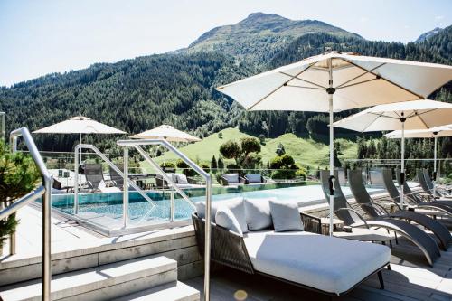 a pool with chairs and umbrellas next to a mountain at Hotel Arlmont 4 Stern Superior in Sankt Anton am Arlberg
