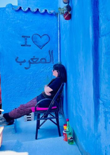 a woman sitting in a chair in front of a blue wall at Vallparadis Pension Familiar" FIRDAUS" in Chefchaouene