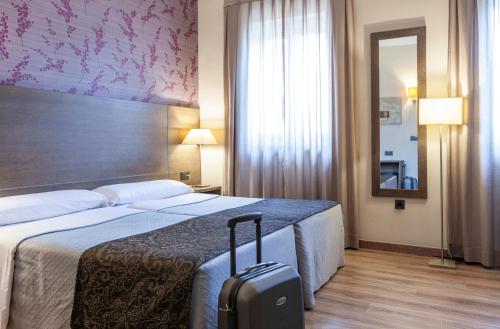 a hotel room with a bed with a suitcase at Hotel Macià Monasterio de los Basilios in Granada