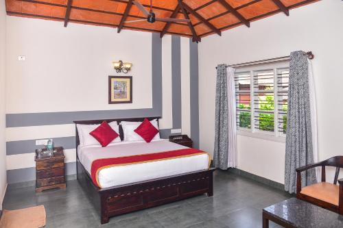 a bedroom with a bed with red pillows and a window at Clover Holiday Village in Madikeri