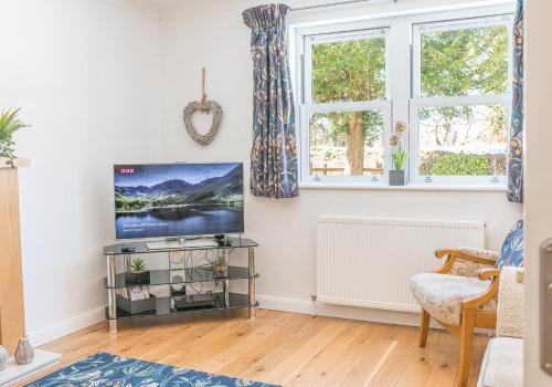 a living room with a flat screen tv and two windows at Riverside View in Keswick