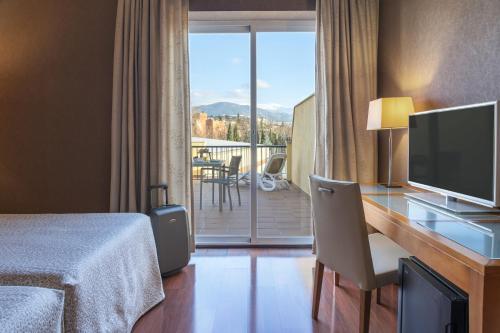 Habitación de hotel con escritorio, TV y balcón. en Hotel Macià Monasterio de los Basilios en Granada