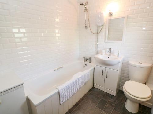 a white bathroom with a toilet and a tub and a sink at Beach Way Cottage in Gorran Haven
