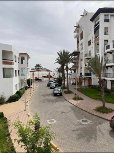 a street with parked cars and palm trees next to buildings at Apartement Marina Zina, Agadir in Agadir