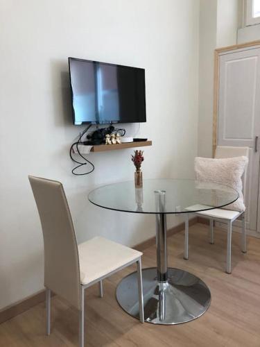 une table en verre avec deux chaises et une télévision murale dans l'établissement Charmant studio à 2 pas de Monaco., à Beausoleil