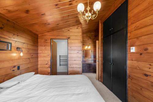a bedroom with wooden walls and a bed with a chandelier at Lakefront Gem - Kuratau Holiday Home in Kuratau