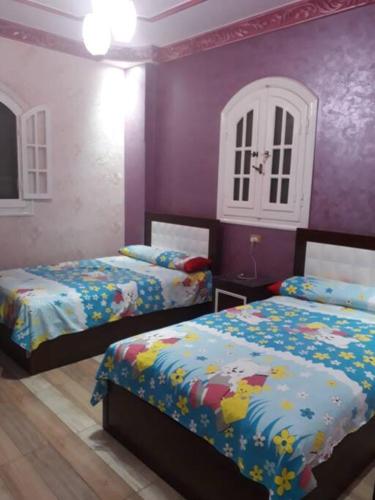 a bedroom with two beds and purple walls at Rental apartment at Ras El Bar City in ‘Izbat al Jirabī
