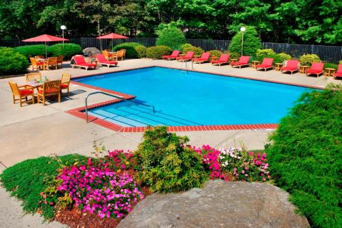 una piscina con sillas, mesas y flores en Trumbull Marriott Shelton en Trumbull