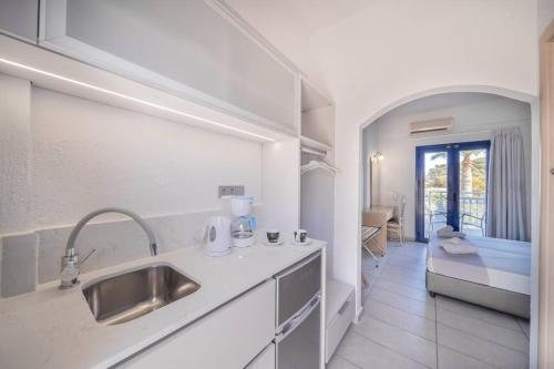 een witte keuken met een wastafel en een slaapkamer bij Sergiani Garden Hotel Apartments in Stalida