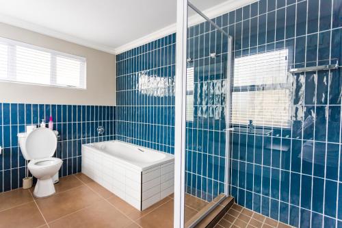 a blue tiled bathroom with a tub and a toilet at Blue Yellow Door Home in Port Elizabeth