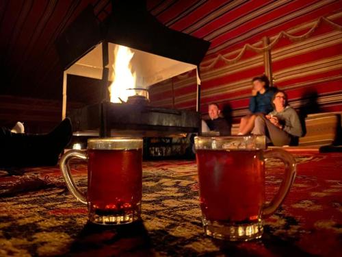 two glasses of beer sitting on a table in front of a fire at Golden Sands Camp in Wadi Rum