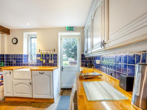 a kitchen with white cabinets and blue tiles on the walls at Islington Hall in Tilney All Saints