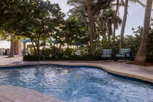 a swimming pool with two chairs and palm trees at Marriott's Oceana Palms in Palm Beach Shores