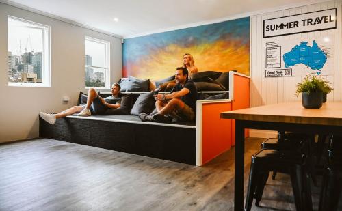 a group of people sitting on a bed in a room at Nate's Place Backpackers Sydney in Sydney