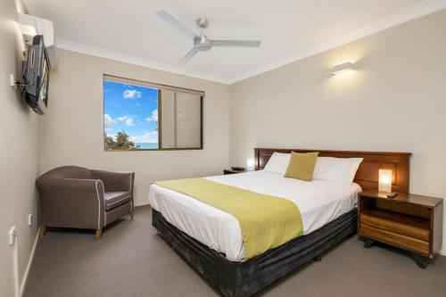 a bedroom with a bed and a chair and a window at L'Amor Holiday Apartments in Yeppoon
