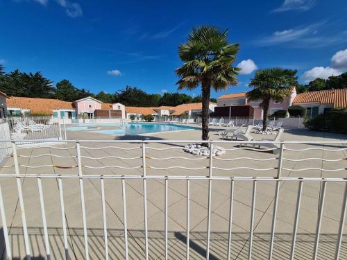 une clôture en face d'une piscine avec un palmier dans l'établissement Maison avec Piscine Chauffée, Terrasse et Parking à 300m de l'Océan - FR-1-224C-219, à Saint-Hilaire-de-Riez