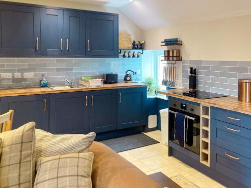 una cocina con armarios azules y un sofá en una habitación en Taigh Violet Rose, en Gramisdale