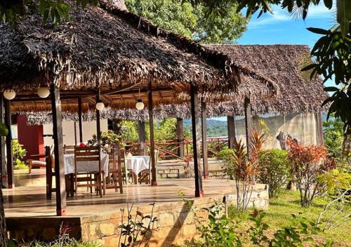 a wooden deck with a table and a thatch roof at WINGS HOTELS in Nosy Be