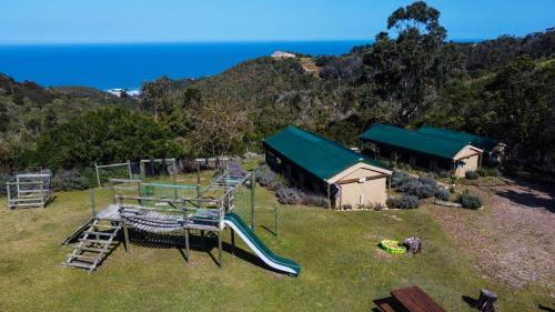 a playground with a slide and a building and the ocean at Trees&Seas - Glamping with farm animals in Wilderness