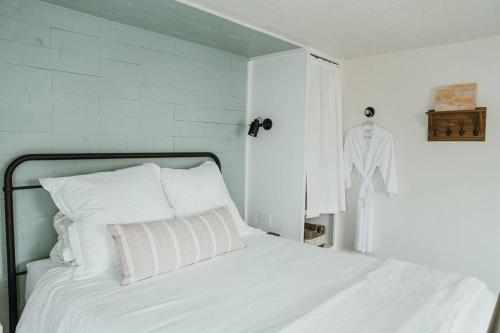 a white bed with white pillows and a shirt hanging on a wall at Charming Cuvée Cottage, 2 blocks to downtown! in Carlton