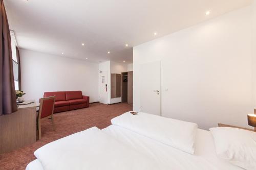 a hotel room with two beds and a red couch at Hotel Excelsior Dortmund Hauptbahnhof in Dortmund