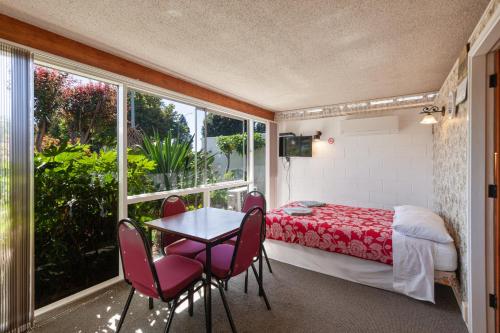 een kamer met een tafel en stoelen, een bed en een raam bij Aaryn Court Motel in Rotorua