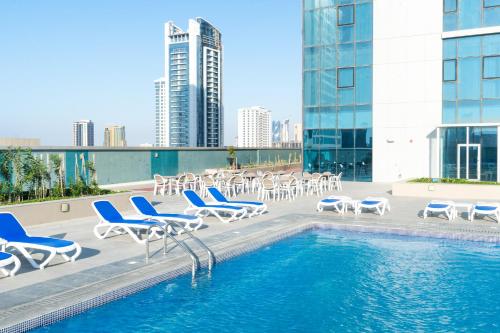 S Plaza Suites Hotel في Seef: حمام سباحة مع كراسي صالة تشايس ومجموعة من الفيزور