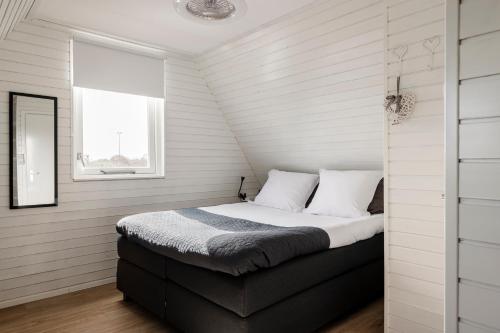 a bedroom with a bed with white walls and a window at Strandhuis de Zeeparel met hottub in Petten