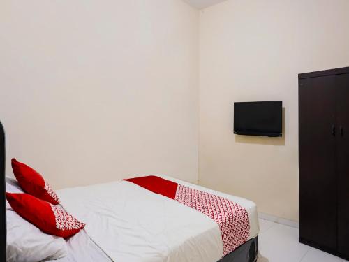 1 dormitorio con 1 cama con almohadas rojas y TV en OYO 92451 Hasan House Syariah 2, en Nagoya
