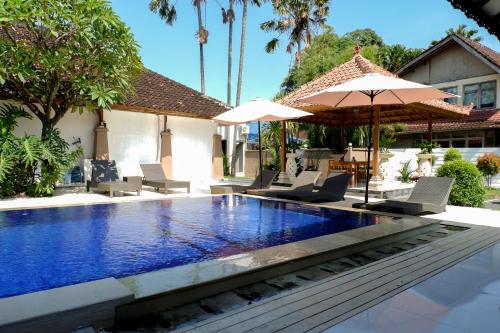 a pool with chairs and umbrellas next to a house at Puri Panca Jaya Hotel in Seminyak
