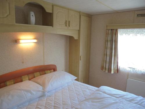a bedroom with a bed with white sheets and a window at Seaways : The Westmorland SW:- 6 Berth, Enclosed Veranda in Lincolnshire