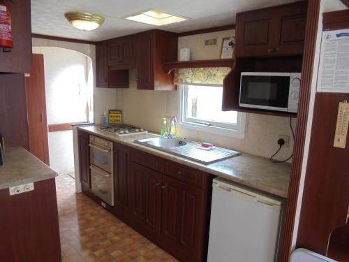 a kitchen with wooden cabinets and a sink and a microwave at Seaways : The Westmorland SW:- 6 Berth, Enclosed Veranda in Lincolnshire