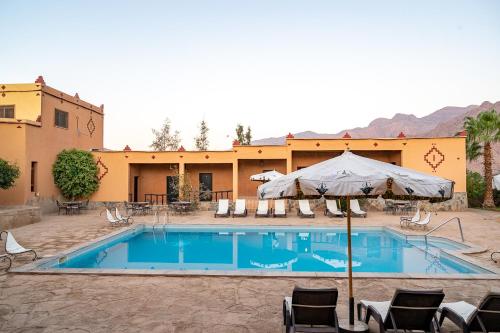 einem Pool mit Stühlen und einem Sonnenschirm vor einem Gebäude in der Unterkunft Auberge Kasbah Chez Amaliya in Tafraout