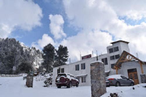 twee auto's geparkeerd voor een gebouw in de sneeuw bij Heavess Peak Hotel in Muzaffarabad