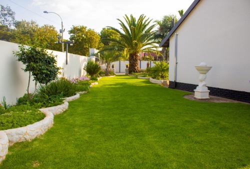 een tuin met groen gras en een wit gebouw bij Mint Guesthouse in Randfontein