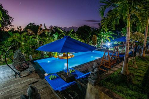 a swimming pool with blue chairs and an umbrella at Tatak Bunut Villa Ceningan in Nusa Lembongan