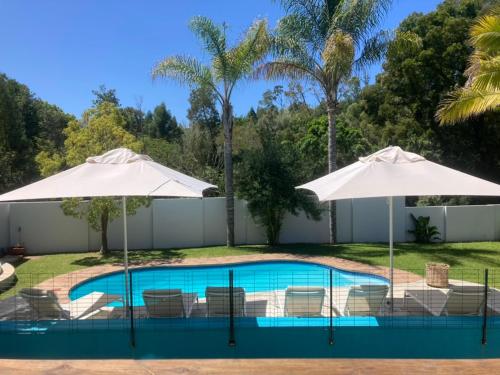 a swimming pool with two umbrellas and chairs at Tonquani - Knysna (est. 2022) in Knysna