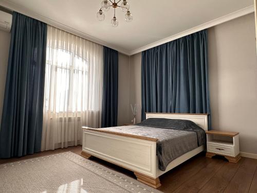 a bedroom with a bed with blue curtains and a chandelier at Aikol in Bishkek