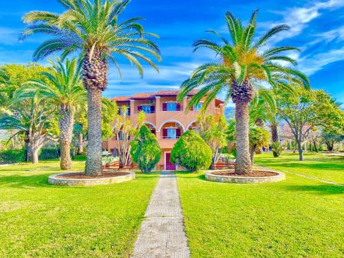 un camino bordeado de palmeras frente a un edificio rosa en Villa Pami en Almiros Beach