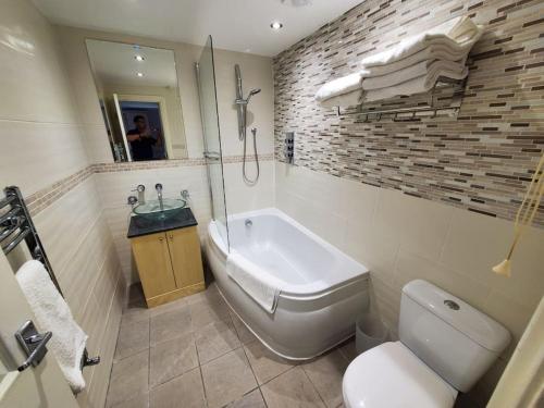 a bathroom with a tub and a toilet and a sink at Central Windsor 2 bedroom flat with free parking in Windsor