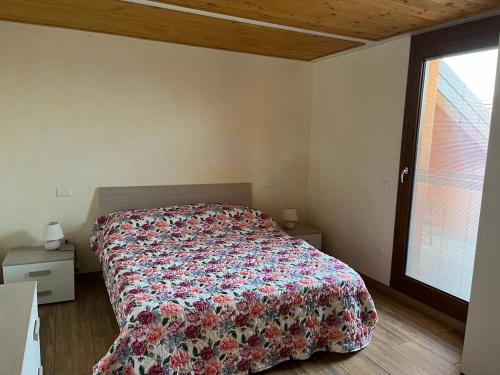 a bedroom with a bed with a floral bedspread and a window at Perla Top Floor Apartment in Sirmione