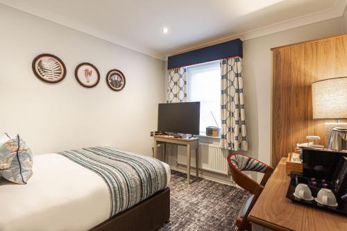 a hotel room with a bed and a desk and a television at The Manor Coastal Hotel & Inn, Blakeney - The Coaching Inn Group in Blakeney