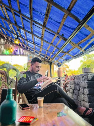 a man sitting at a table reading a book at Dreamwoods A travellers farm in Dharamshala