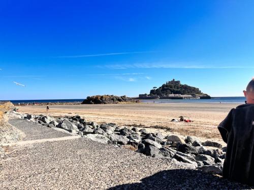 a person sitting on a beach with a castle in the distance at Syds Corner bell tent in St. Just