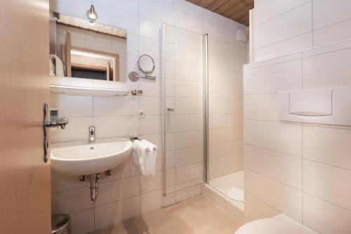 ein weißes Bad mit einem Waschbecken und einer Dusche in der Unterkunft Landgasthof Augustiner in Oberstdorf