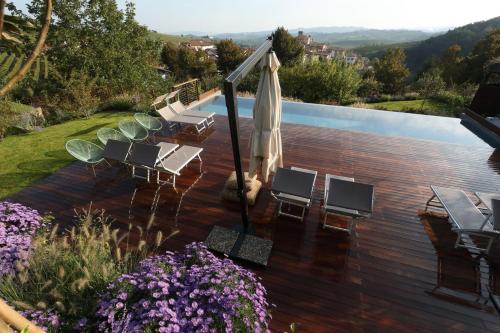 una terraza con sillas y una sombrilla junto a la piscina en Villa Carla Suites in Barolo, en Barolo