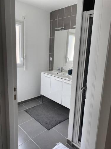 une salle de bain blanche avec un lavabo et un miroir dans l'établissement Belle maison neuve à 5 mn de la plage, à Colleville-Montgomery
