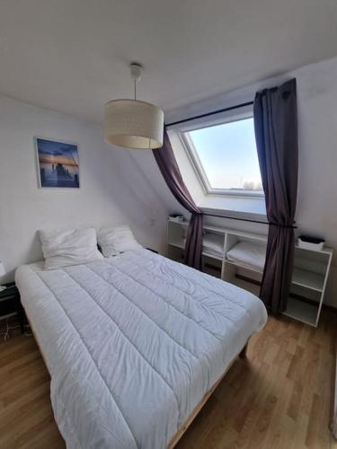 une chambre avec un grand lit blanc et une fenêtre dans l'établissement Bel appartement cosy et lumineux en duplex, à Granville