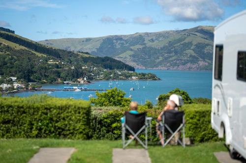 two people sitting in chairs in front of a lake at Akaroa Top 10 Holiday Park in Akaroa