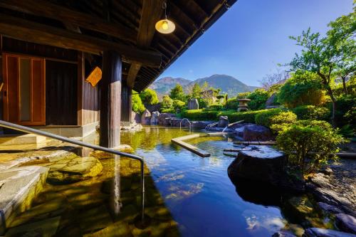 a pool of water next to a building with mountains in the background at 由布の里 旅荘 牧場の家 Ryoso Makibanoie in Yufuin